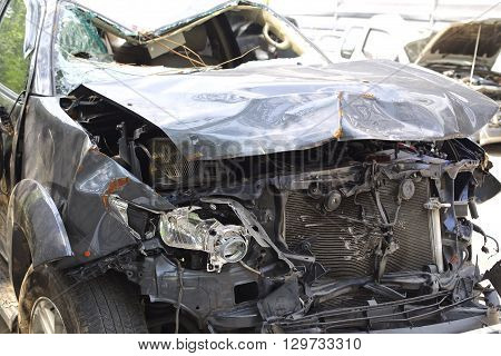 A wrecked car lays in wait after a vicious car accident. Rescue workers linger in the background.