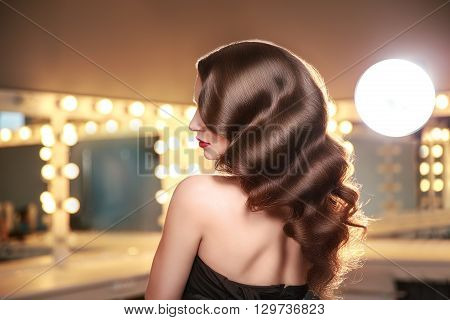 Long curly hair. Back, side view. Brunette in makeup room with studio lights. Portrait.
