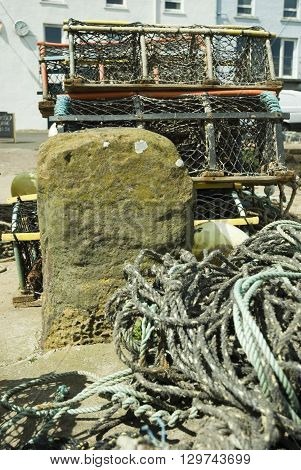 an image of fishing pots and nets on the harbour beside a stone capstan