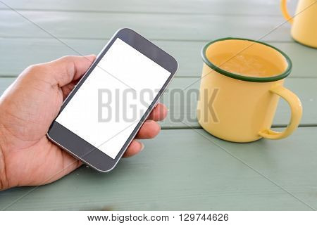 White display Smart phone in handGlass of water made from zinc yellow on wooden table.