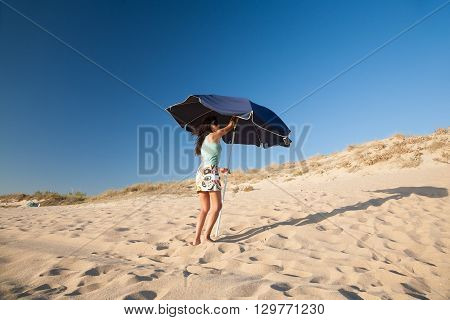 mini skirt and shirt brunette summer vacation woman opening blue parasol in sand dune with blue sky in Palmar beach in Vejer Cadiz Andalusia Spain Europe