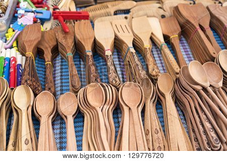 Handmade wooden vintage kitchen utensils for sale at the market. Various wooden kitchen tools. Different wooden tableware. Wooden stand under the hot pan.