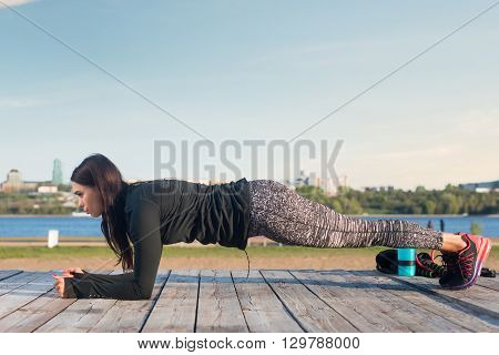 Sporty young woman doing elbow plank exercise working on abdominal muscles exercising on the river coast