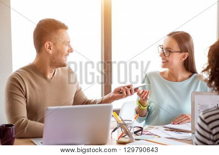 Pleasant interlocutor. Positive cheerful smiling colleagues sitting at the table and talking while working in the office together