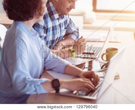 Work in concert. Pleasant delighted positive colleagues sitting at the table and using laptops while working in the office