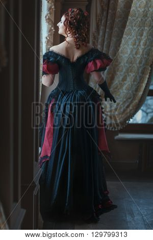 Woman in Victorian dress standing back at the window.