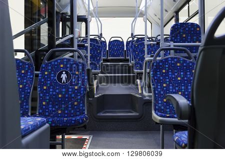 Bus inside, city transportation white interior with blue seats in row, retirement places, open doors, handles for standing passengers, bright lights and air conditioner
