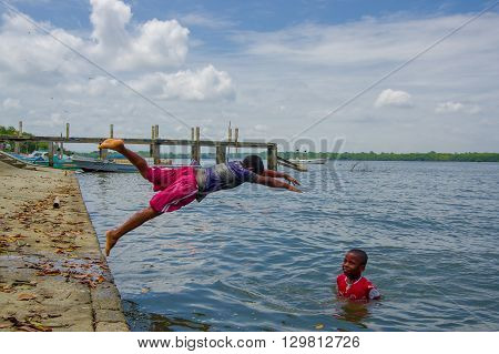 Muisne, Ecuador - March 16, 2016: Kids diving and swimming in pacific ocean from stone surface with clothes on.
