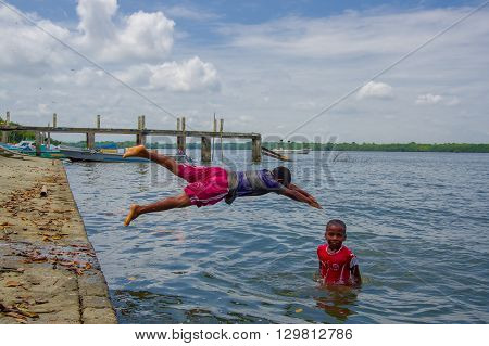 Muisne, Ecuador - March 16, 2016: Kids diving and swimming in pacific ocean from stone surface with clothes on.
