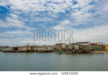 Muisne, Ecuador - March 16, 2016: Muisne town as seen from water, modest wooden houses sitting on poles waterfront pacific ocean, city buildings background and beautiful blue sky.