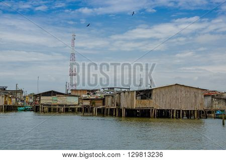 Muisne, Ecuador - March 16, 2016: Muisne town as seen from water, modest wooden houses sitting on poles waterfront pacific ocean, city buildings background and beautiful blue sky.