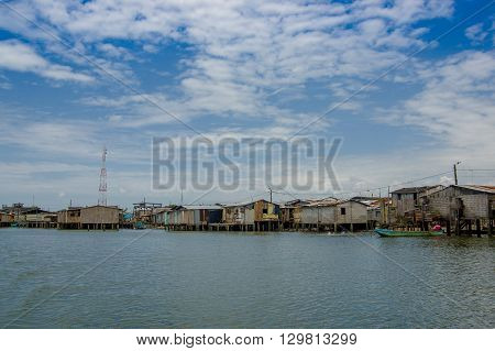 Muisne, Ecuador - March 16, 2016: Muisne town as seen from water, modest wooden houses sitting on poles waterfront pacific ocean, city buildings background and beautiful blue sky.