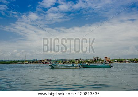 Muisne, Ecuador - March 16, 2016: Traditional fishing boats tied together at sea, city in background and beautiful blue sky.