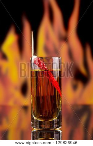 Red chili peppers in a glass of vodka on a background of flames.