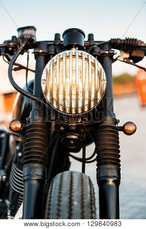 One vintage custom motorcycle cafe racer motorbike with grill headlight on empty rooftop parking lot during sunset. Hipster lifestyle student dream. Lamp is on and directed to camera.