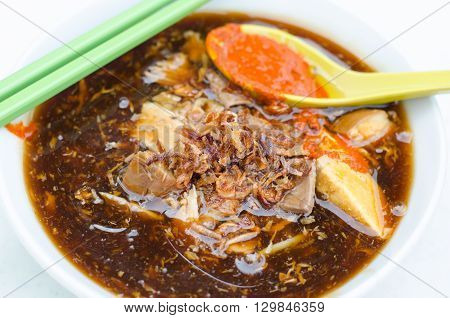 A bowl of Loh mee with chopsicks and a spoonful of chili paste