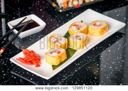 Sushi roll with scallop and Tomago on white plate on blabk table
