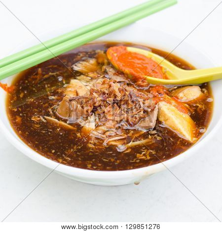 A bowl of Loh mee with chopsicks and a spoonful of chili paste