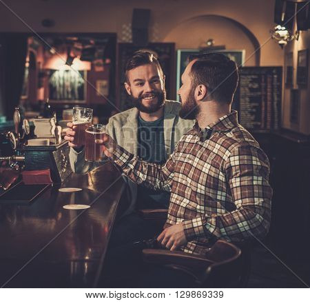 Cheerful old friends having fun and drinking draft beer at bar counter in pub.