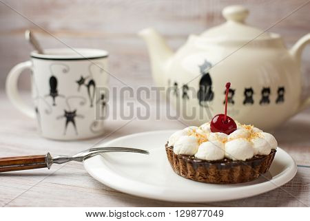 Cup tea and cake with a cherry on the table