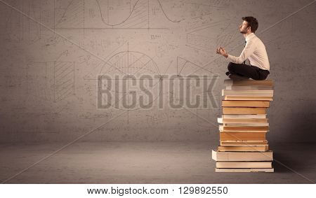 A serious businessman in suit sitting on a pile of giant books in front of a greyish brown wall with drawn lines, angles, numbers, circles and curves.