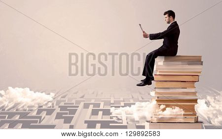 A businessman with laptop tablet in elegant suit sitting on a stack of books on top of sandy labirynth background concept