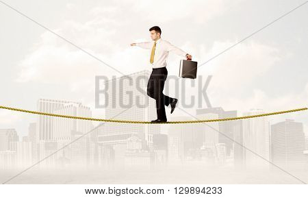 A young elegant businessman walking on tight golden rope in front of city buildings landscape background concept