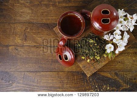 Japan's tea cups with green tea on wooden plank and sakura flowers on dark wooden background