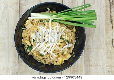 Thai fried noodle in black bowl with bean sprouts and Garlic chives on topping. Pad Thai in a black bowl put on wood table.