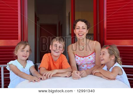 Женщина с тремя детьми сидит в номере на веранде стол с белой скатертью и смеется