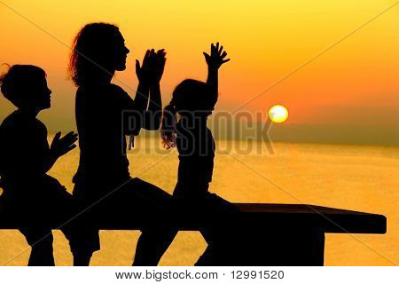 Mor med to børn sidder på bænken på stranden på sunset og lystigt slam hænder