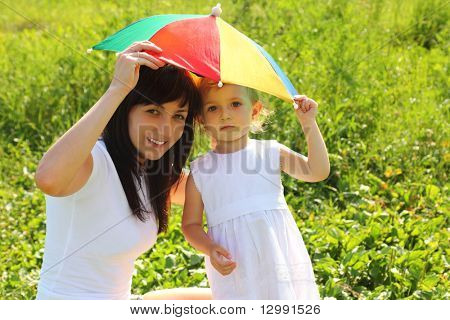 Mãe e filha escondem-se sob um guarda-chuva do sol