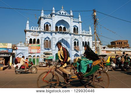 LUCKNOW, INDIA - DEC 18, 2012: Cycle rickshaw takes an elderly Muslim woman on a beautiful street with blue houses on December 18, 2012 in Lucknow, India. Lucknow in Uttar Pradesh state has pop. of 4588455