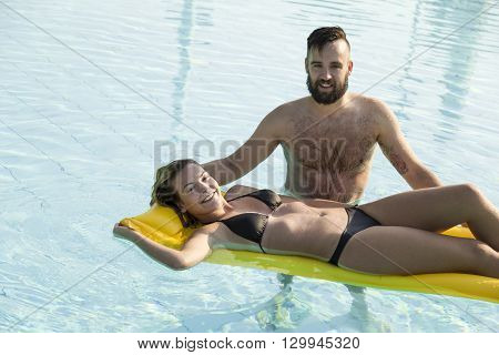 Young handsome man pulling his girlfriend through the swimming pool on an airbed