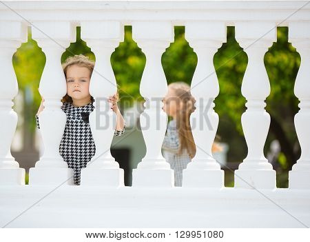 Happy little girls playing on the street. Hiding behind balister
