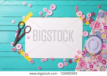 Sewing thread - buttons scissors fabric and empty tag on turquoise wooden background. Selective focus. Scrapbboking. Flat lay. Place for text.