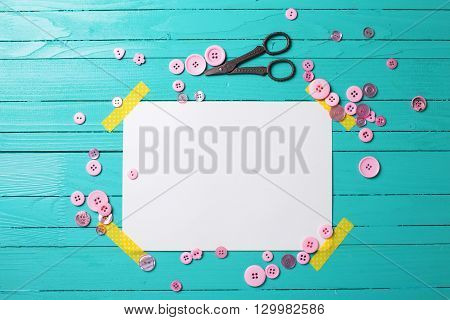 Sewing thread - buttons scissors and empty tag on turquoise wooden background. Selective focus. Scrapbboking elements. Flat lay. Place for text.
