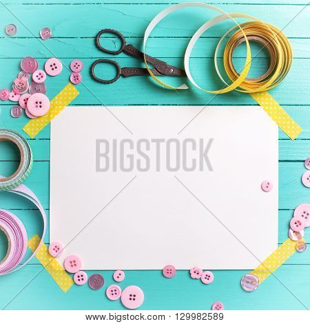 Sewing thread - buttons scissors ribbon and empty tag on turquoise wooden background. Selective focus. Scrapbboking. Flat lay. Place for text. Toned image.