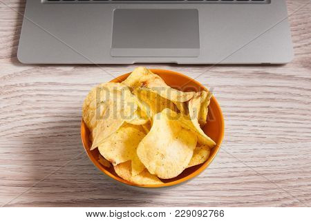 Laptop And Bowl Of Chips On Wood Table. Bad Habits Concept