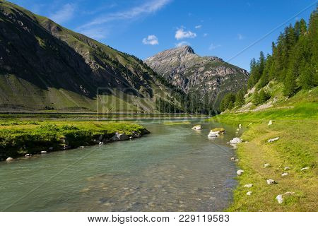 Spol River Flowing In Lake Livigno, Corno Brusadella Mountain Background