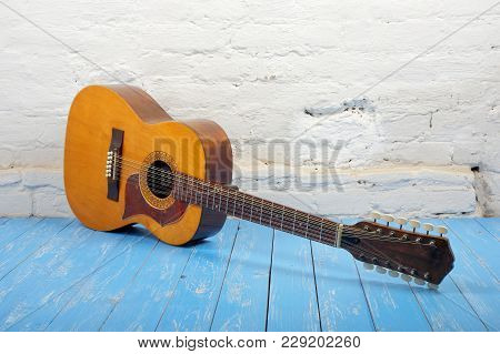 Musical Instrument - Vintage Twelve-string Acoustic Guitar On A Brick Background And Blue Wooden Flo