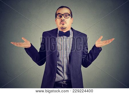 Young Man In Formal Clothing Shrugging Shoulders While Posing On Gray And Looking Confused.