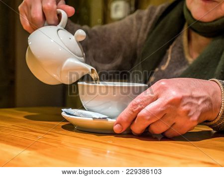 Closeup View Tea Pot Pouring Drink Into Cup In Senior Hands.
