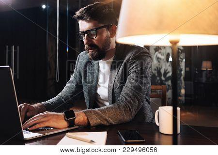 Man Using Contemporary Mobile Notebook. Bearded Businessman Working At Night In Modern Loft Office. 