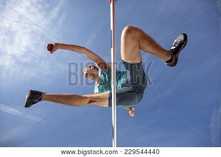 Low Angle View Of Determined Male Athlete Jumping Over A Hurdles.