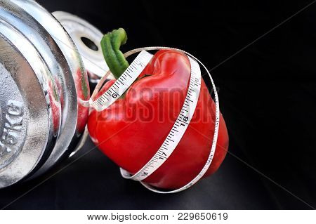 Diet Concept,measuring Tape Curl Up On A Red Sweet Pepper With Silver Dumbbell On Black Background.c