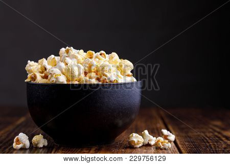 Popcorn In A Ceramic Bowl And Scattered On A Wooden Background.