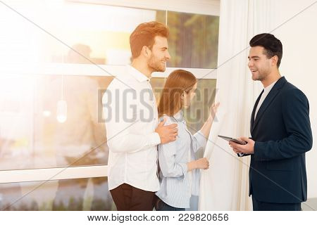 Young Couple In A Meeting With A Realtor. A Guy And A Girl Make A Contract With A Realtor About Buyi