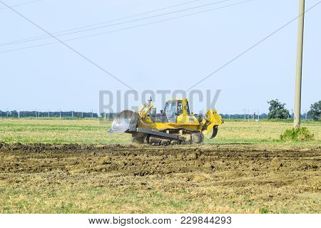 Russia, Temryuk - 15 July 2015: The Yellow Tractor With Attached Grederom Makes Ground Leveling. Wor