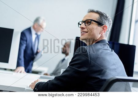 Selective Focus Of Smiling Businessman In Eyeglasses Looking Away In Office